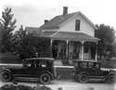 People on front porch with two cars parked in front, Young America, circa 1915