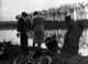 Three people at river's edge, with bicycle in foreground